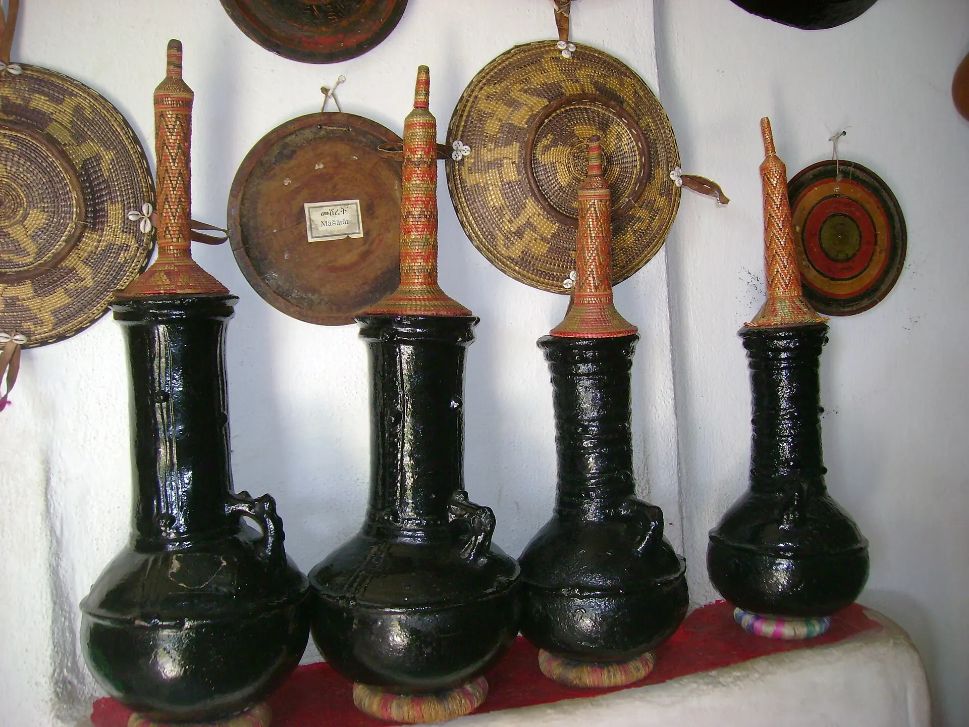 Black clay coffee pots and woven Harari baskets displayed on a white wall in Harar