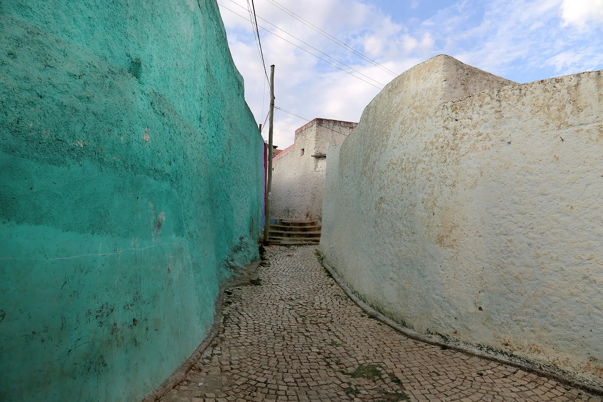 A narrow, curving lane between turquoise and white walls in old Harar