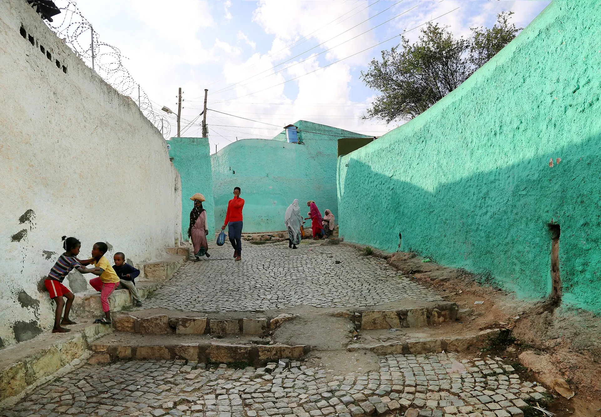 A cobbled lane between green and white walls in Harar's old town, children playing